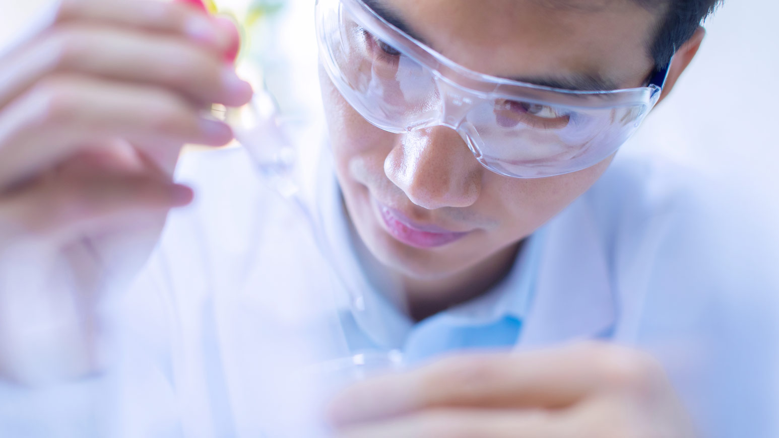 Man met veiligheidsbril en witte jas die een pipet vast heeft