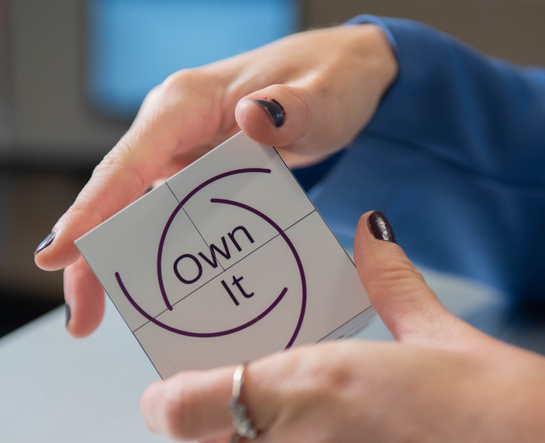 Twee handen die kubus vasthouden waarop “Own It” staat afgebeeld