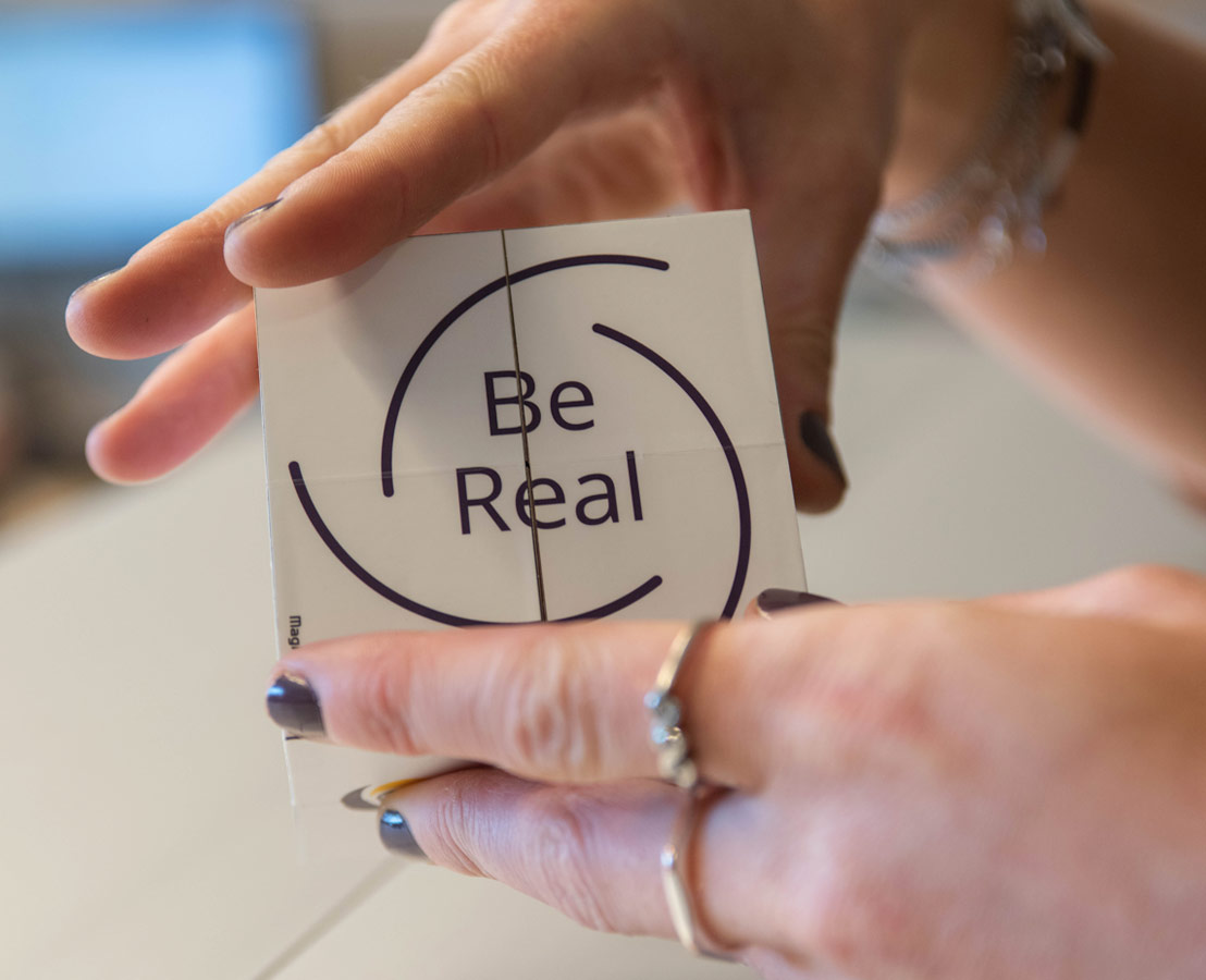 Twee handen die kubus vasthouden waarop “Be Real” staat afgebeeld