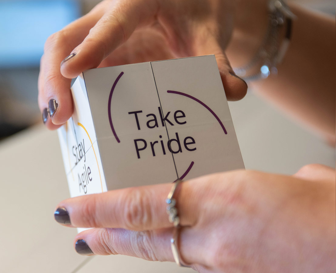 Twee handen die kubus vasthouden waarop “Take Pride” wordt afgebeeld 
