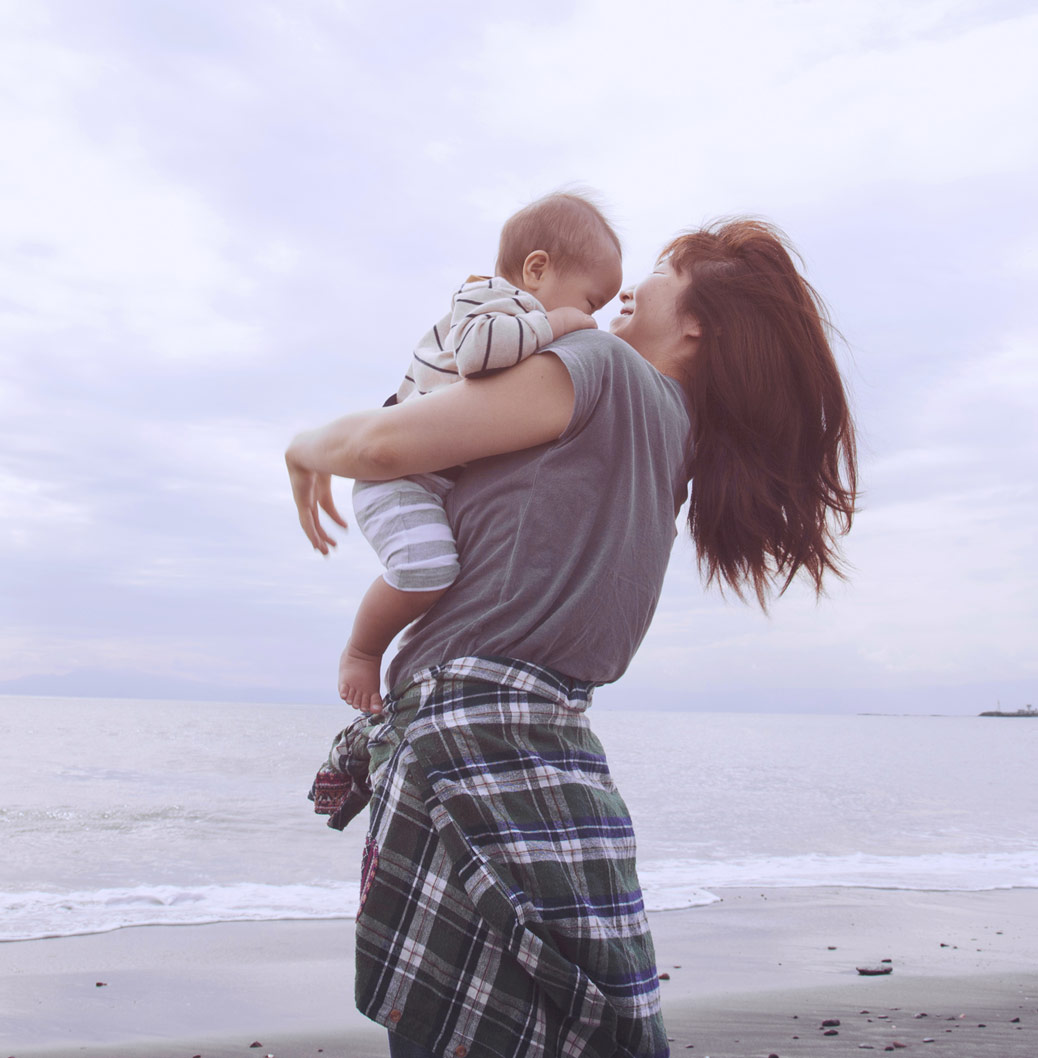 A woman carrying a baby on the beach